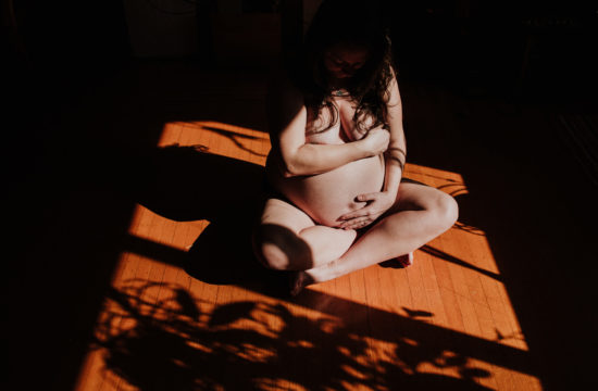 dark and moody maternity photo, photo of a pregnant woman sitting naked in sunshine